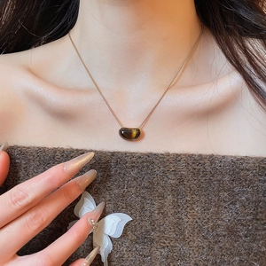 Detail of tiger eye pendant necklace on model with brown off-shoulder sweater