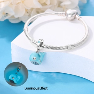 Detailed view of glowing whale charm with blue enamel on silver snake chain bracelet