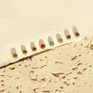 Detailed view of eight colorful zircon stud earrings arranged on a textured white paper edge