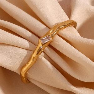 Detail of 18K gold irregular textured cuff bracelet with rectangular zircon on silk cloth