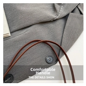 Close-up of brown leather handle on gray suit fabric with neat stitching and button