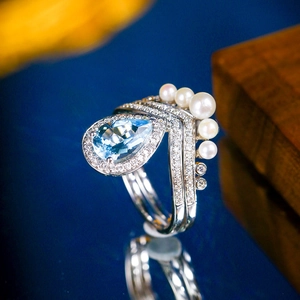 Macro detail of pear-cut blue gemstone ring with pave diamonds and five gradient pearls