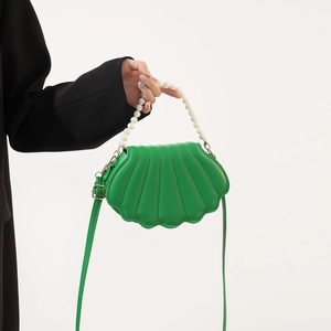 Detail of green shell-shaped crossbody bag with pearl handle and pleated texture