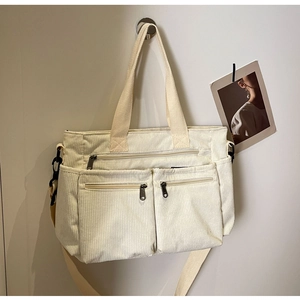 Detail of off-white corduroy tote bag showing textured fabric and front zipper pockets