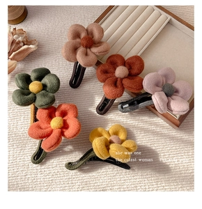 Close-up of six colorful plush flower hair claws in autumn shades on a soft fabric background