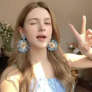 Close-up of retro blue and white raffia petal earrings with golden center on model