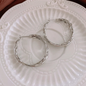 Macro detail of silver twisted geometric hoop earrings on vintage ceramic plate