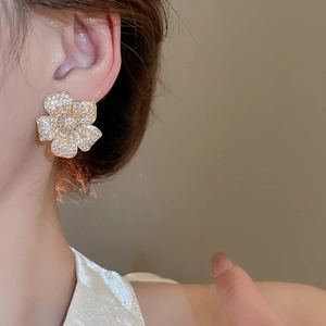 Close-up of sparkling zircon flower stud earring worn on ear with gold plating
