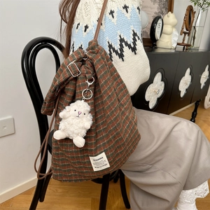 Plaid corduroy bucket bag with drawstring and plush sheep charm on a vintage chair