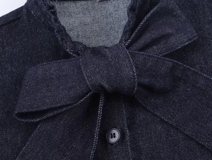 Close-up detail of dark blue denim shirt featuring a decorative bow and black button