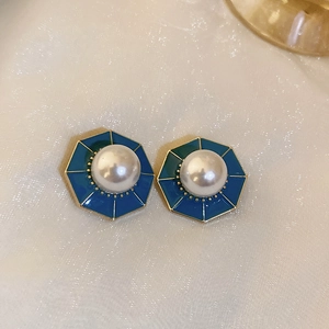 Detailed close-up of octagonal gold-edged blue enamel earrings with a central pearl
