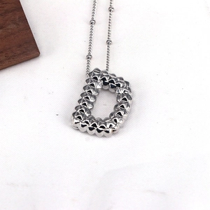 Macro detail of silver necklace featuring a textured letter D pendant with rivet patterns