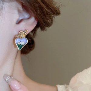 Détail de boucles d'oreilles cœur vintage avec émail violet et perles sur l'oreille