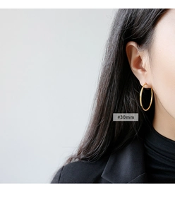 Side view detail of a model wearing a 30mm golden minimalist hoop earring in S925 silver