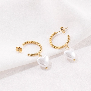 Détail des boucles d'oreilles torsadées dorées en C avec une perle blanche en cœur