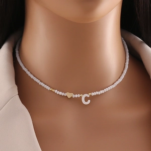 Detail of beaded necklace with gold heart and C pendant on model neck