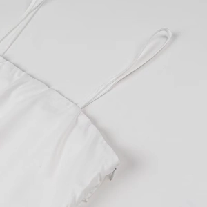 Detailed view of white pleated dress showing side hidden zipper and thin strap