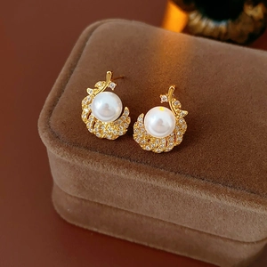 Close-up of gold feather-shaped earrings with white pearls and sparkling zircons