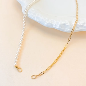 Asymmetric necklace featuring white pearls and golden paperclip chain on a ceramic plate