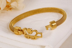 Detail of gold mesh bracelet featuring MOM charm with heart and crown on white fabric