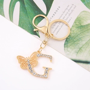 Detailed view of a gold letter G keychain with sparkling crystals and a hollow butterfly charm