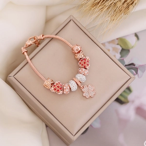 Detail of rose gold charm bracelet with red heart, zircon sphere, and clover pendant