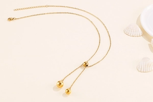 Detail of gold Y-shaped necklace with spherical beads and lobster clasp on beige decor
