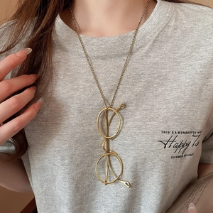 Close-up of minimalist gold glasses pendant necklace worn on a casual grey t-shirt