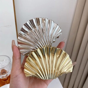 Detailed close-up of glossy gold and silver scallop shell hair claws held by hand