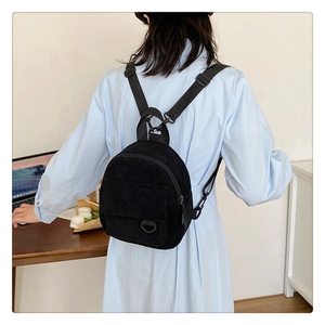 Detail of a black corduroy mini backpack featuring an adjustable strap and a front flap pocket