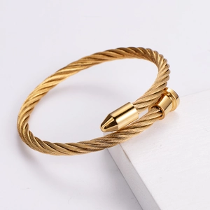 Detailed close-up of golden twisted rope nail bracelet on white stone surface