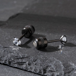 Macro view of 3mm round zircon stud earrings in black steel on textured stone background