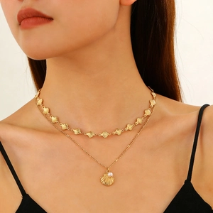 Dettaglio collana a due strati in oro con ciondoli a conchiglia, stella e perla bianca