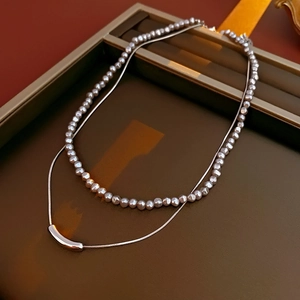 Detail of layered jewelry featuring white pearl strand and sleek silver snake chain