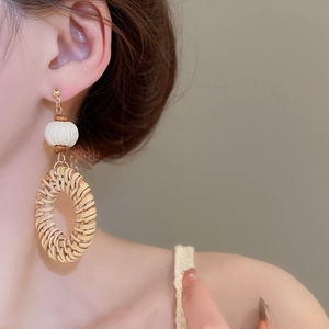 Macro detail of bohemian woven rattan earrings with white beads on model ear
