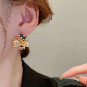 Elegant gold bee earrings with zircon and green gemstone on a model's ear