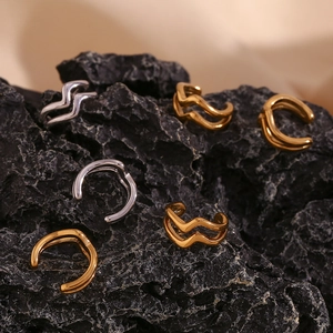 Detailed view of gold and silver double-layer wavy ear cuffs on a dark stone background