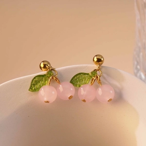 Close-up of sweet cherry earrings with pink round beads and green leaves on ceramic bowl