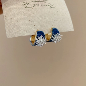 Detail of denim C-shaped earrings with silver starburst studs on a gold metal base