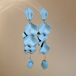 Close-up of matte light blue petal tassel earrings on a minimalist acrylic stand