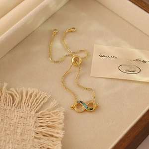 Gold adjustable infinity bracelet with shell inlay and white crystals on wooden jewelry box