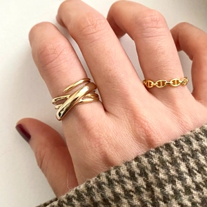 Detailed close-up of a wide braided gold ring and an anchor chain ring worn together