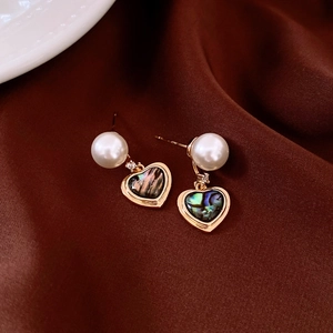 Détail de boucles d'oreilles cœur en nacre irisante et perles sur velours rouge