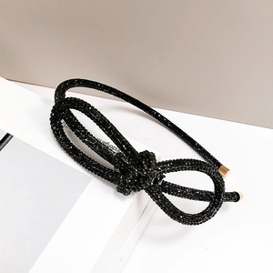 Detail of black rhinestone headband with double bow design and golden metal tips