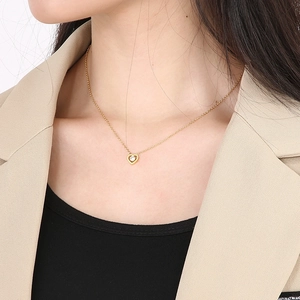Close-up of gold hollow heart necklace with zircon stone on model with beige blazer
