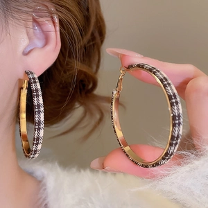 Détail de boucles d'oreilles créoles dorées avec tissu pied-de-poule marron et blanc