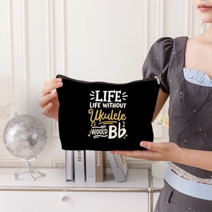 Black canvas cosmetic bag with ukulele theme print held by a person in a cozy setting