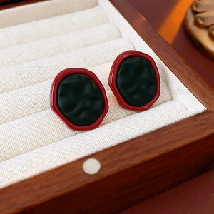 Vue macro de boucles d'oreilles géométriques irrégulières rouges et noires dans un écrin
