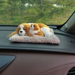Close-up of realistic plush sleeping dogs on a gray mat on a car dashboard decoration