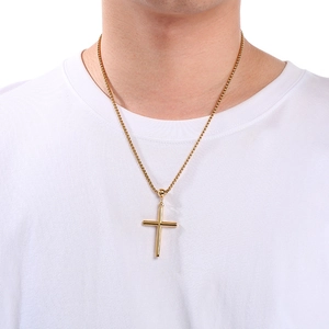 Close-up of a minimalist gold cross pendant with a box chain worn on a white t-shirt
